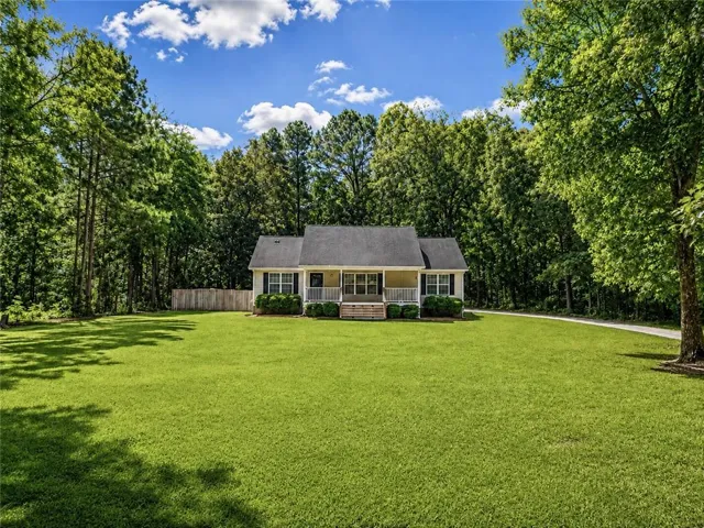 Expansive front lawn, mature perimeter trees, front porch with white railings, dark shingle roof, and light-colored siding