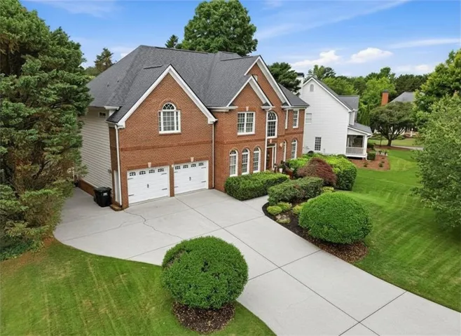 Brick exterior residence with a two-car garage, concrete driveway, and mature landscaping