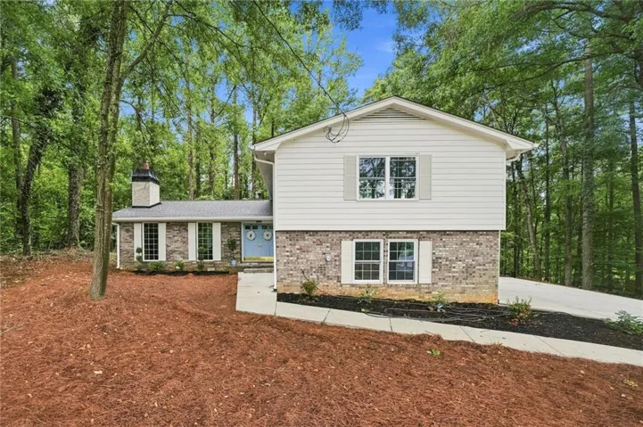 Split-level residence featuring a brick and siding exterior, a light blue entry door, and white window shutters