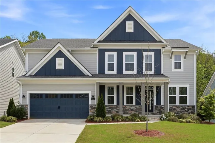 Two-story residential exterior featuring mixed siding, a stone facade, an attached garage, a covered front porch, and a concrete driveway