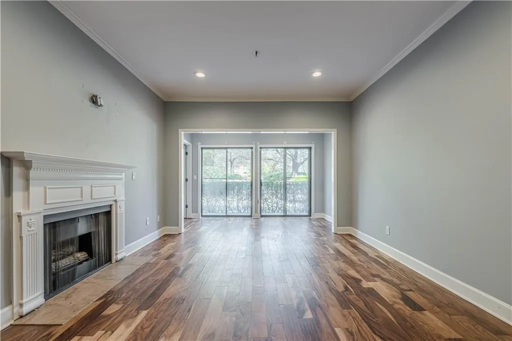 Unfurnished living room featuring baseboards, a fireplace with flush hearth, wood finished floors, and crown molding