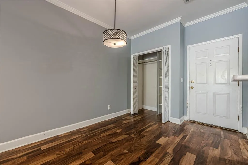 Unfurnished bedroom featuring baseboards, a closet, ornamental molding, and dark wood-type flooring