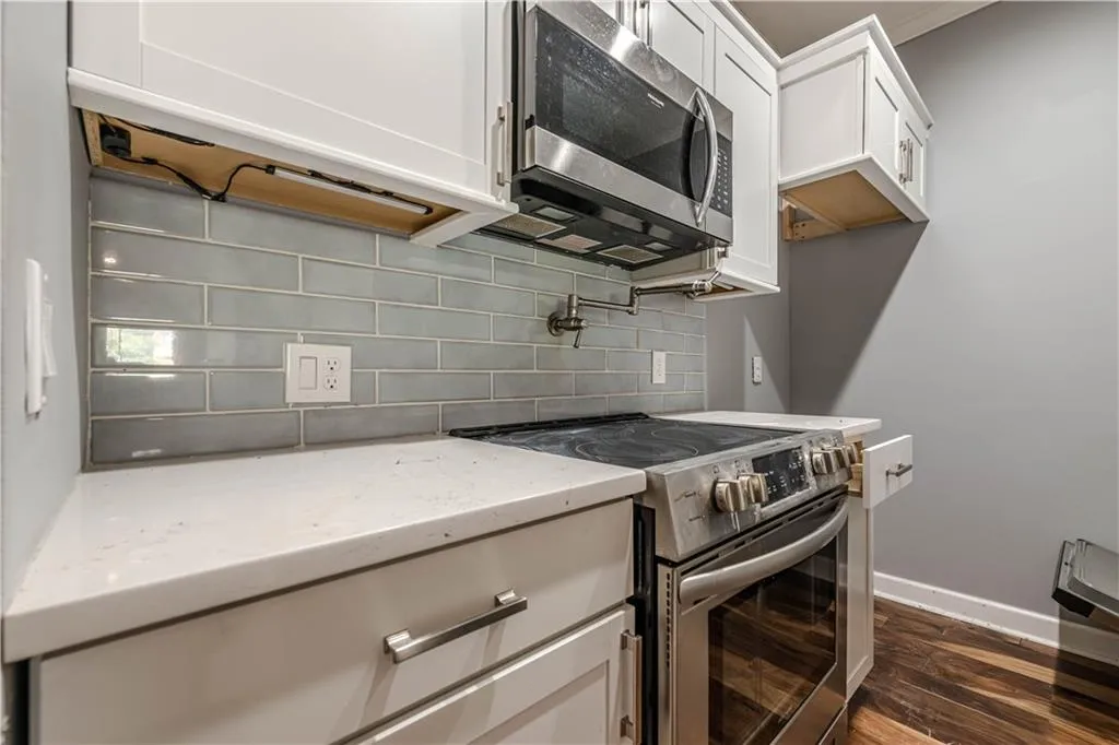 Kitchen featuring light stone countertops, dark wood finished floors, appliances with stainless steel finishes, white cabinetry, and backsplash