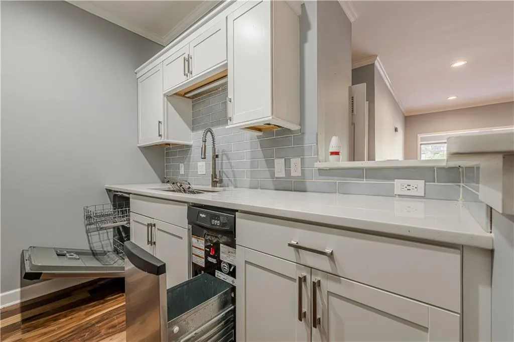 Kitchen with a sink, white cabinetry, backsplash, and ornamental molding