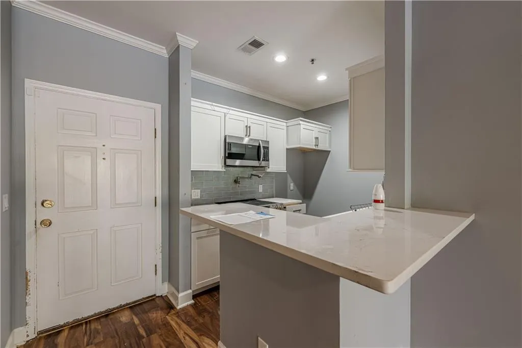 Kitchen featuring visible vents, a peninsula, stainless steel microwave, white cabinetry, and dark wood-style floors