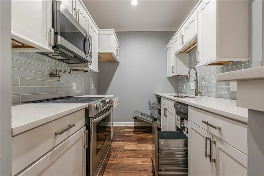 Kitchen with a sink, white cabinetry, dark wood finished floors, stainless steel appliances, and ornamental molding