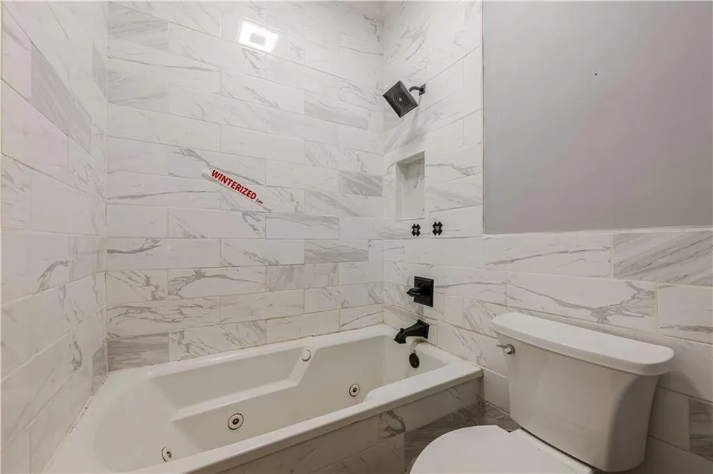 Bathroom with a combined bath / shower with jetted tub, toilet, and tile walls