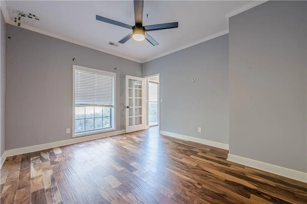 Unfurnished room with crown molding, wood finished floors, baseboards, visible vents, and ceiling fan