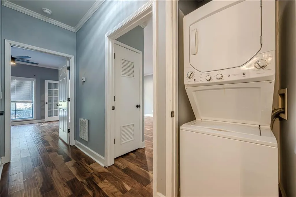 Washroom with dark wood-style flooring, ornamental molding, stacked washer / drying machine, and visible vents