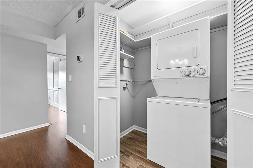 Laundry room featuring dark hardwood / wood-style flooring, a textured ceiling, and stacked washing maching and dryer