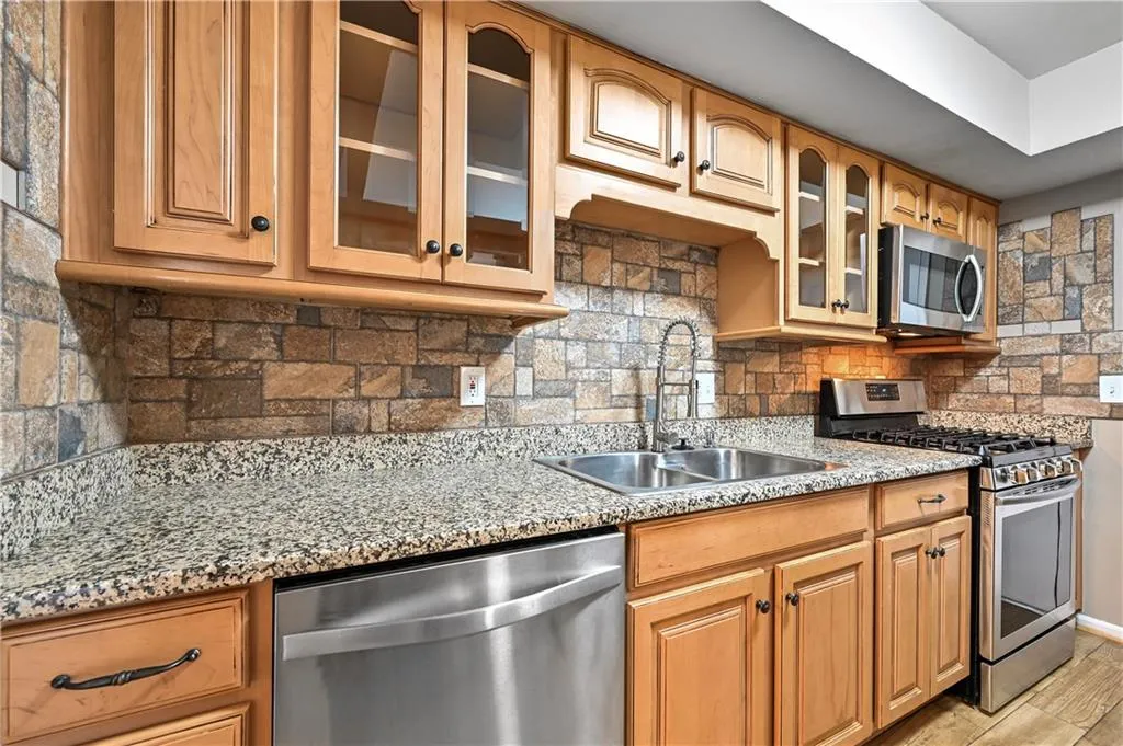 Kitchen with light stone counters, appliances with stainless steel finishes, sink, and backsplash