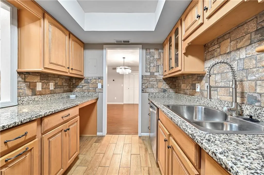 Kitchen with light hardwood / wood-style floors, a raised ceiling, sink, and decorative backsplash