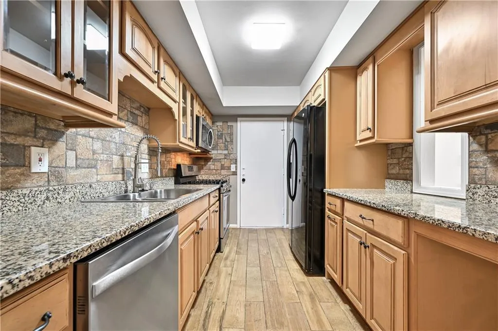 Kitchen with appliances with stainless steel finishes, sink, decorative backsplash, light stone counters, and light hardwood / wood-style floors