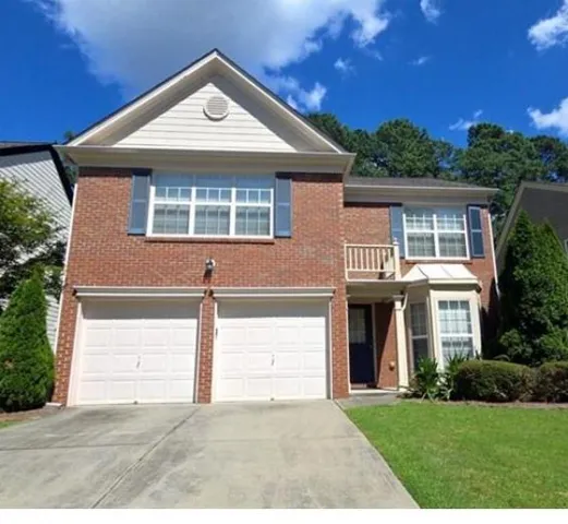 Brick facade residence featuring a two-car garage, bay window, and a gabled roofline with a vent