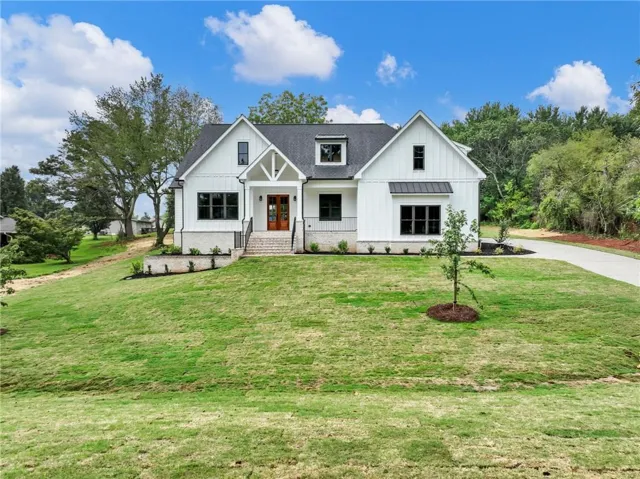 Modern farmhouse exterior with white vertical siding, black-framed windows, and a black shingle roof