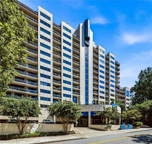 High-rise building with a tiered architectural design, featuring multiple private balconies, blue-tinted windows, and a prominent exterior elevator shaft