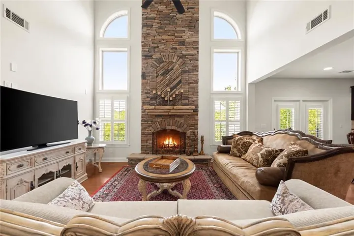 Vaulted living area featuring a floor-to-ceiling stone fireplace, plantation shuttered windows, and hardwood flooring