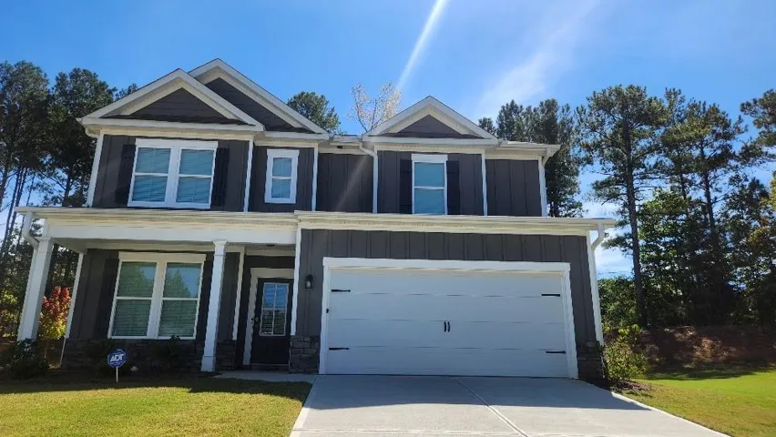 Two-story residence featuring a covered front porch, a two-car garage, and dark siding with stone accents