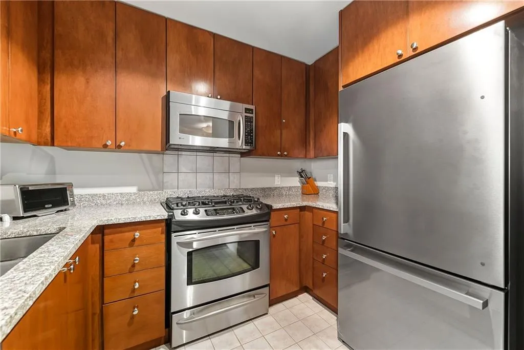 Kitchen featuring wood cabinetry, stainless steel appliances, speckled countertops, and a tiled backsplash