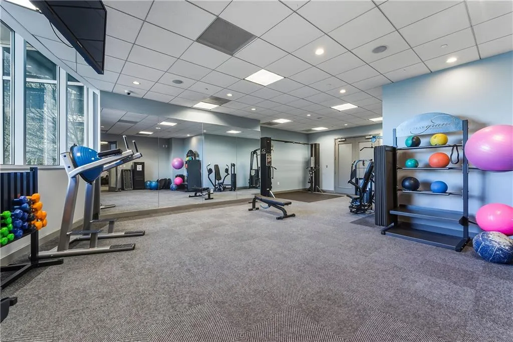 Fitness center with expansive mirrored wall, large windows, recessed lighting, and patterned carpet flooring