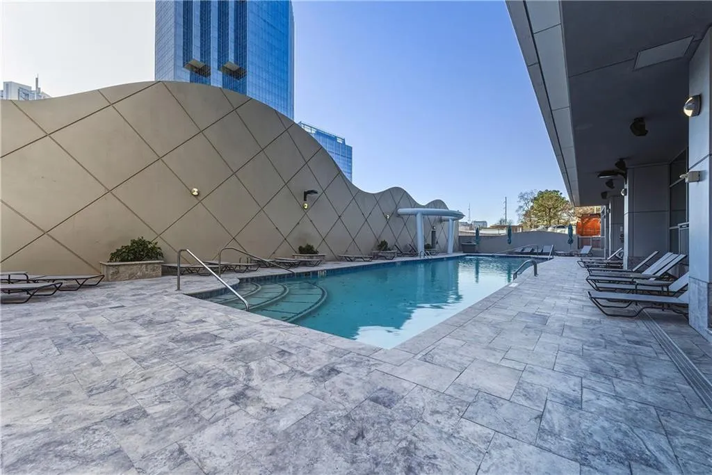 Outdoor swimming pool with tiled steps, surrounded by stone-look pavers and an architectural wall