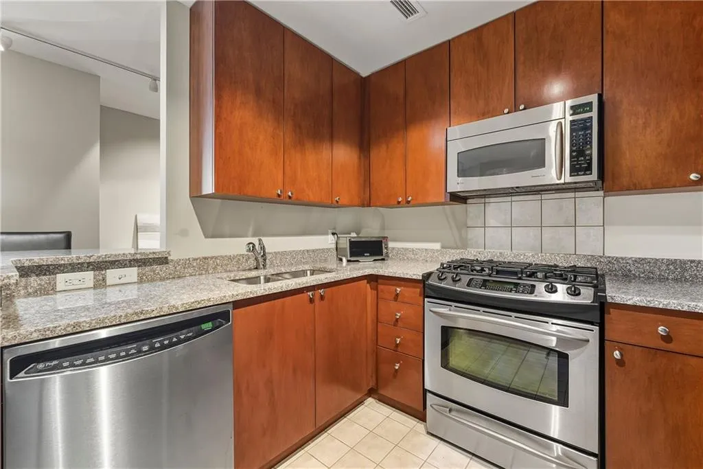 Kitchen featuring stainless steel appliances, wood-finish cabinetry, granite countertops, and a tiled backsplash