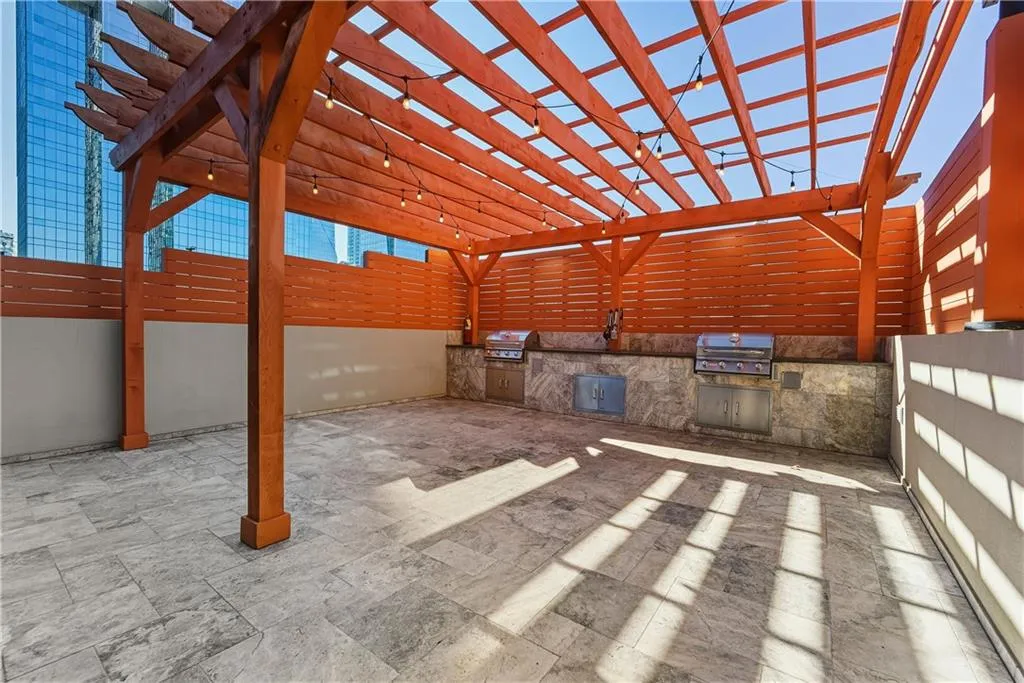 Expansive patio featuring a wood pergola, string lighting, two built-in grills, and natural stone tile flooring