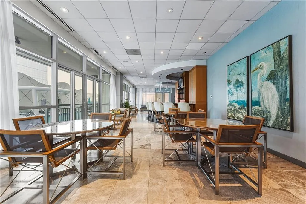 Expansive full-height windows, neutral stone tile flooring, recessed lighting, and a built-in bar with wood-finish cabinetry