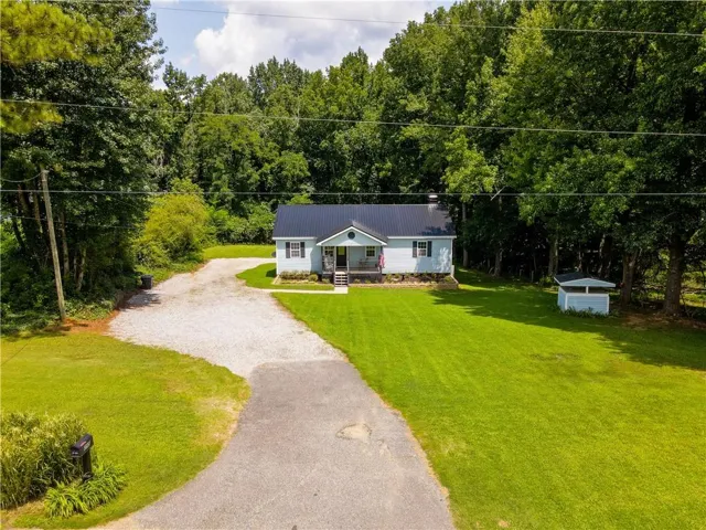 Light blue exterior with a black metal roof, front porch, gravel driveway, and a detached outbuilding