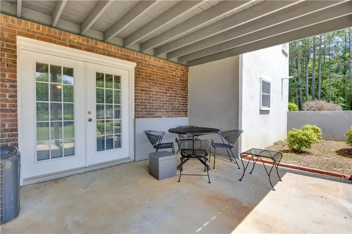 Covered concrete patio featuring white French doors with divided lites, a brick wall, and a stucco exterior