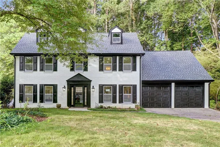 Colonial inspired home with driveway, a garage, roof with shingles, a front yard, and brick siding