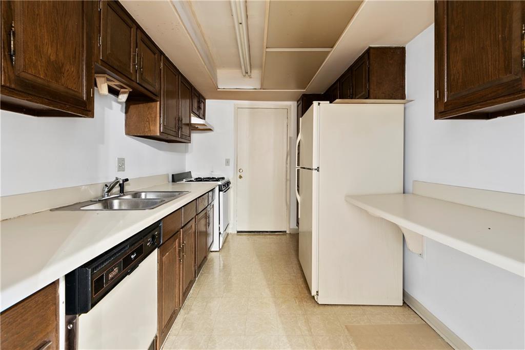 Kitchen featuring light tile flooring, dark brown cabinets, sink, and white appliances