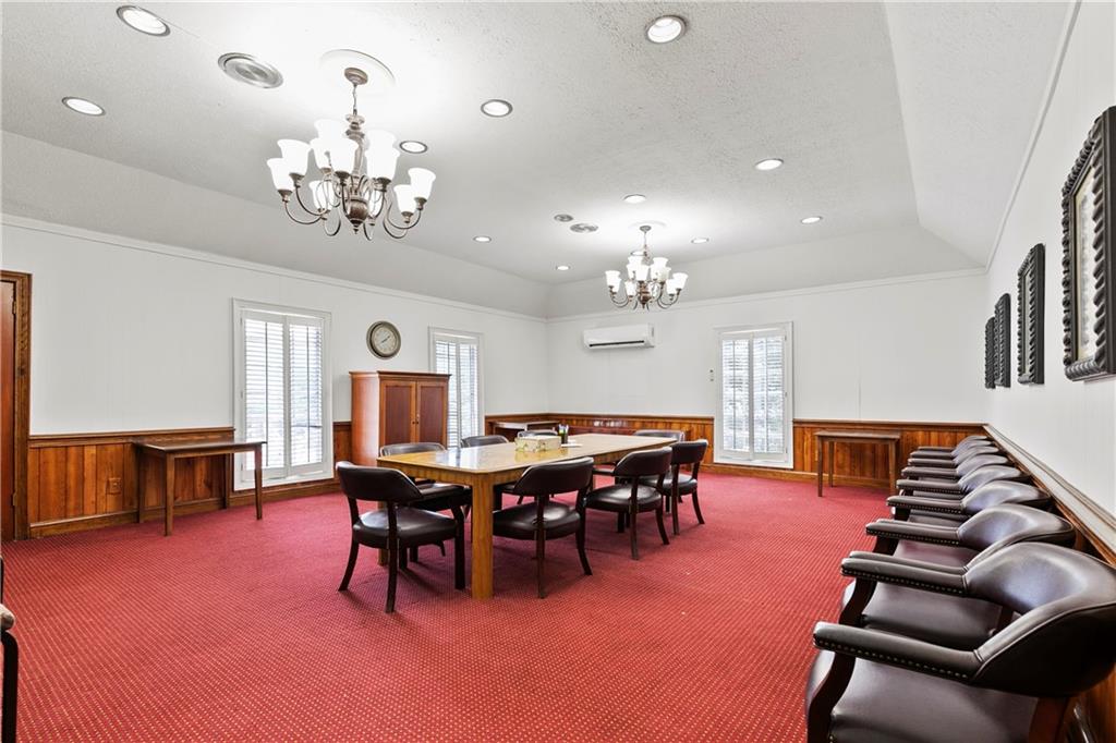 Carpeted dining area with a wall mounted air conditioner, a tray ceiling, and an inviting chandelier