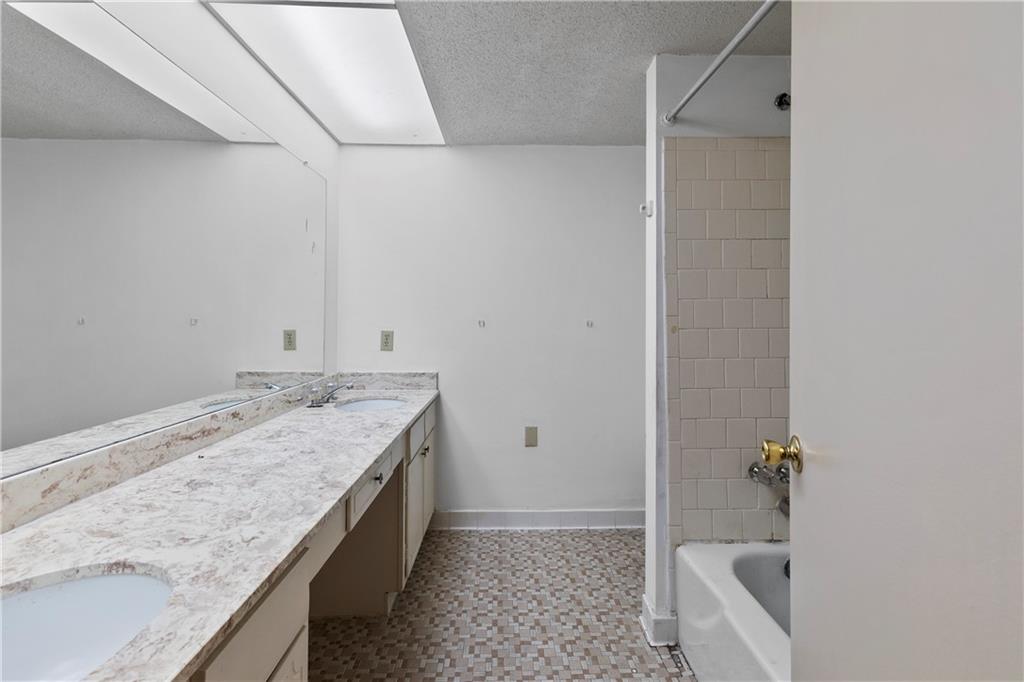 Bathroom featuring tile flooring, double sink vanity, a textured ceiling, and tiled shower / bath