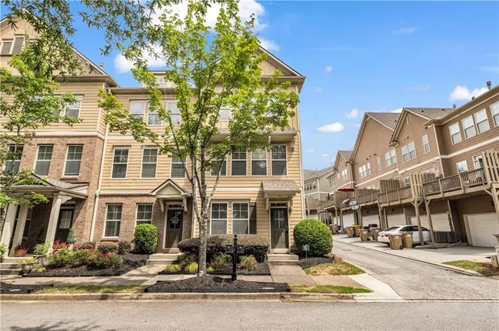 Three-story townhome featuring a brick facade with light-colored siding, a covered entry, and a small front yard with mature landscaping