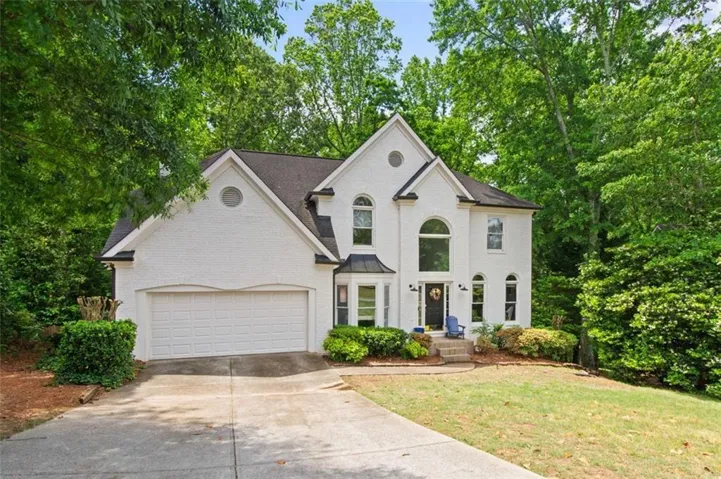 White painted brick exterior with a prominent two-story arched window, a two-car garage, and mature landscaping