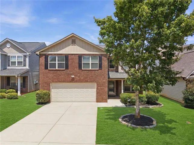Brick exterior with a two-car garage, mature landscaping, and a concrete driveway