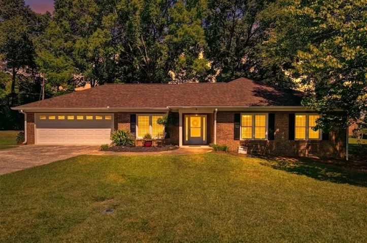 Brick exterior with a brown shingle roof, attached garage with panel doors, and a concrete driveway