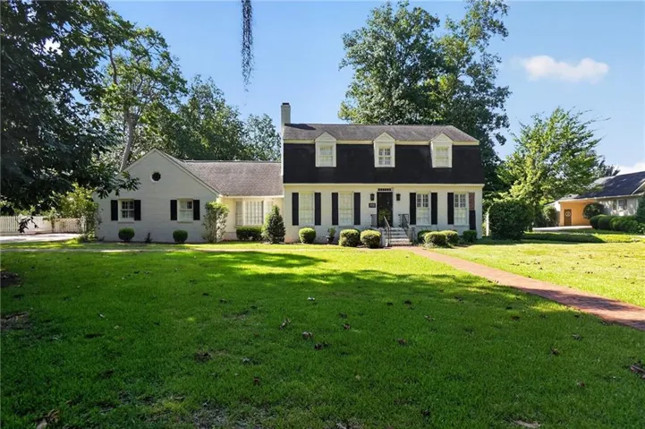 Dormered Dutch Colonial style residence with a prominent front entrance, flanked by traditional shutters and mature plantings