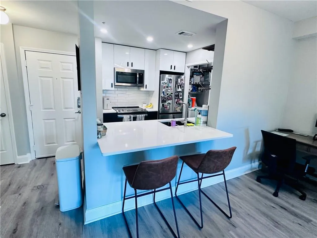Kitchen featuring white cabinetry, decorative backsplash, light wood-style floors, appliances with stainless steel finishes, and a breakfast bar area