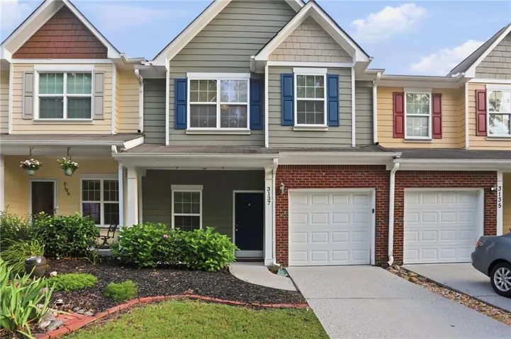 Three-unit townhouse-style property featuring varied siding materials, attached garages, and a manicured front lawn