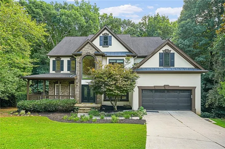 Stucco exterior with stone accents, a covered front porch, an arched entry window, and a dark asphalt shingle roof