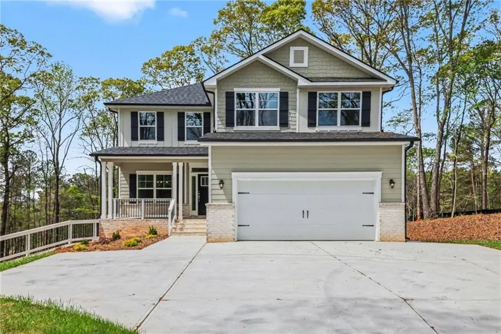 Two-story exterior with a covered porch, attached two-car garage, concrete driveway, and mature perimeter trees