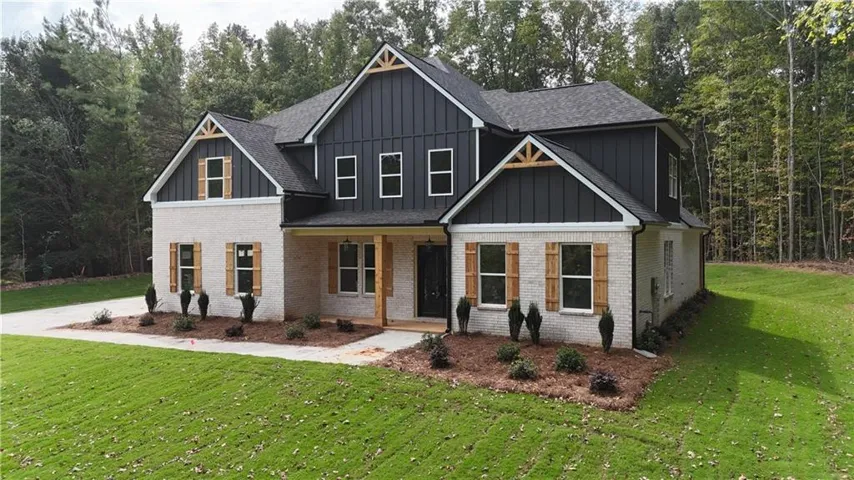 Modern farmhouse exterior featuring light-colored brick, dark vertical siding, dark shingle roof, decorative wood shutters, and a covered entry porch