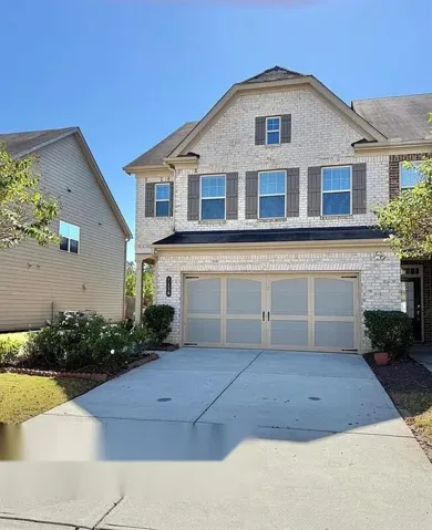 Brick exterior with decorative shutters, integrated two-car garage, concrete driveway, and mature landscaping