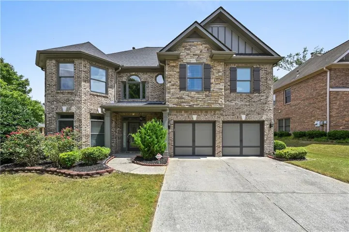 Brick and stone facade with dark shutters, dual garage doors, and a concrete driveway
