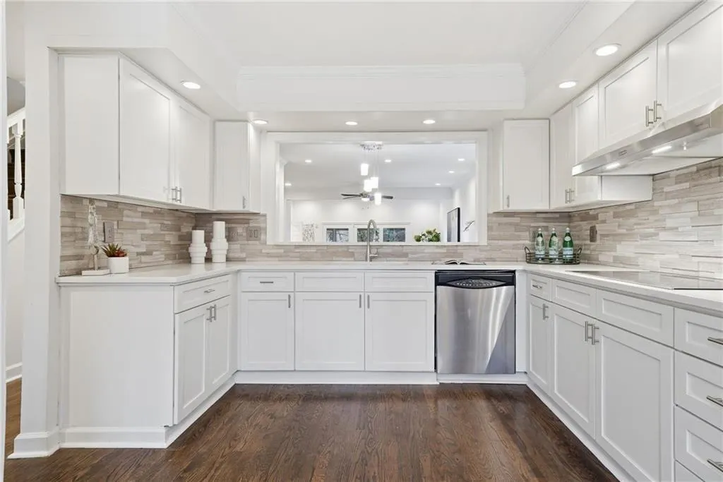 Kitchen featuring white cabinets, dishwasher, under cabinet range hood, crown molding, and dark wood-style floors