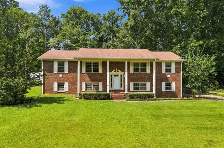 Brick exterior with white shutters, dual-level window placement, columned entryway, and mature surrounding trees