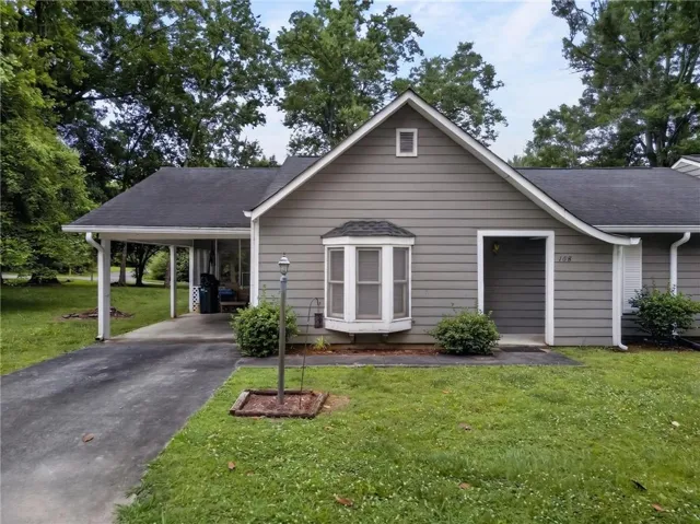 Exterior featuring gray siding, a prominent bay window, a covered carport, and a dark asphalt shingle roof