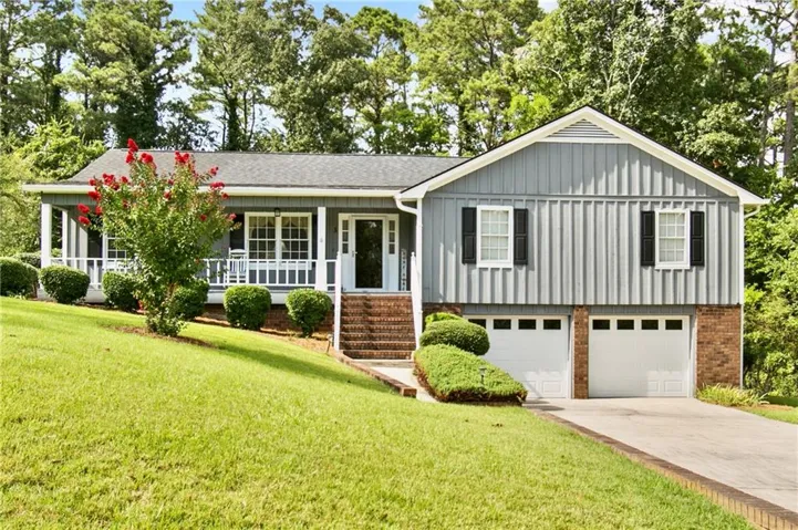 Charming ranch-style home featuring a covered front porch with white columns, gray vertical siding with brick foundation accents, and a two-car garage